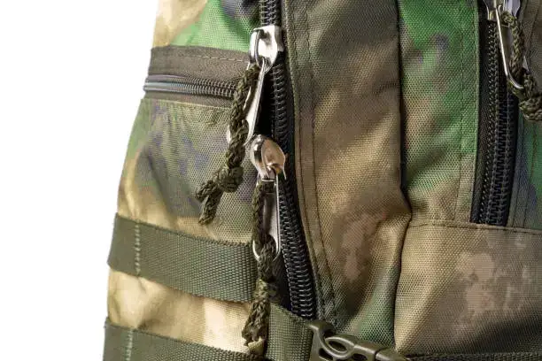 Close-up of a camouflage backpack with zippers, straps, and MOLLE webbing.