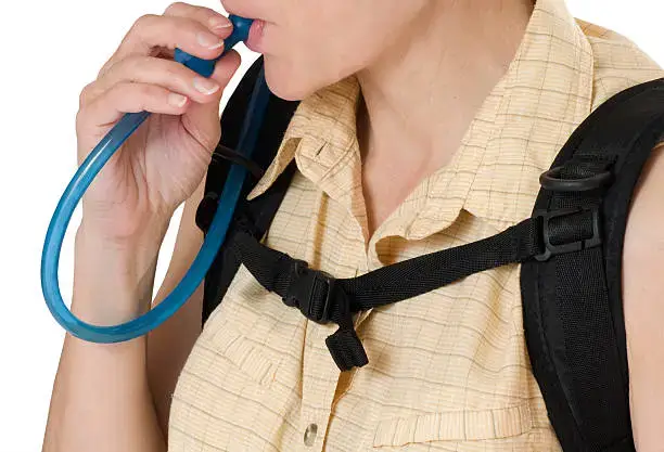 a woman drinking from a hydration hose coming out of the backpack on her back.